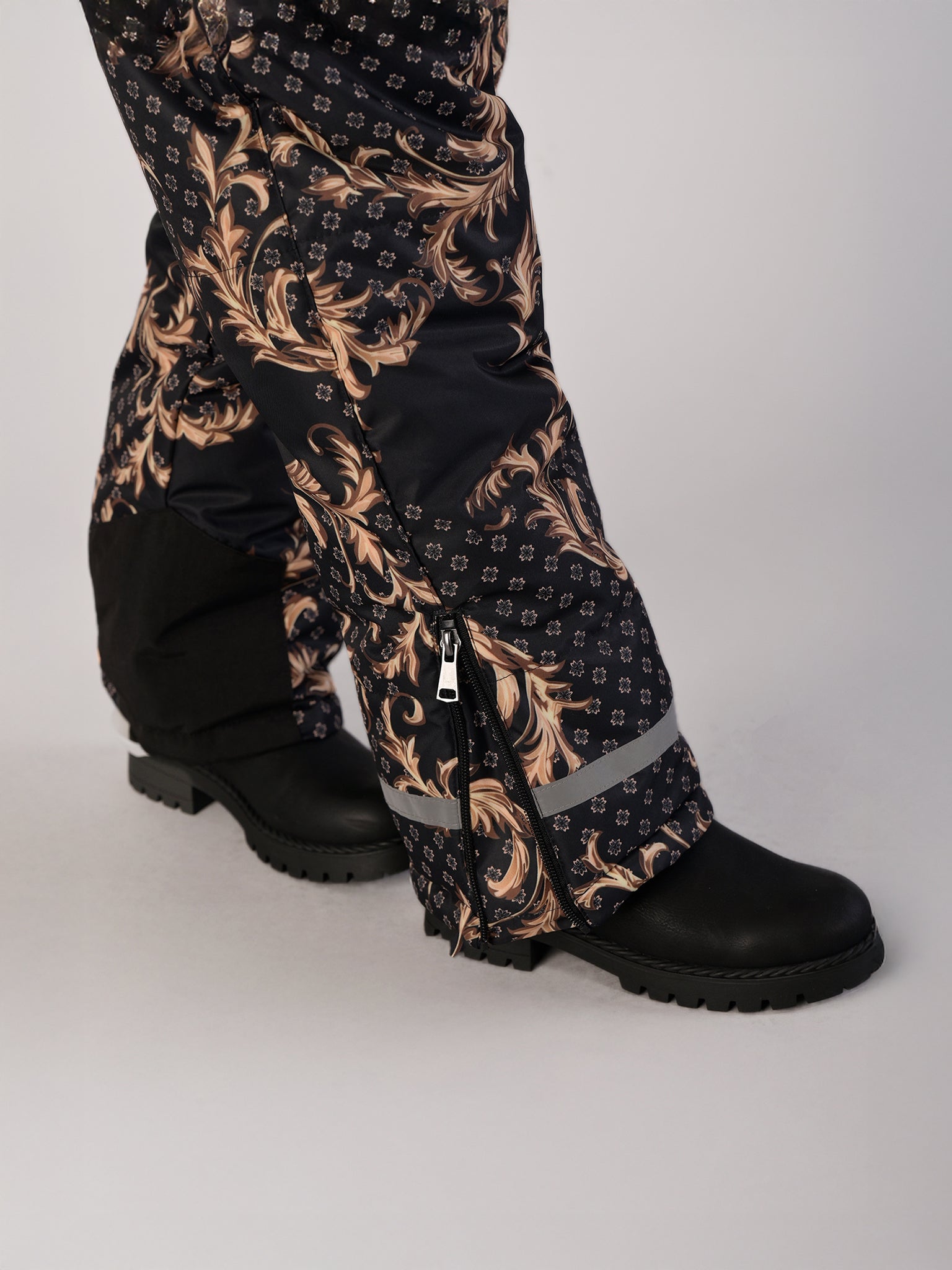 Luxury girls’ snowsuit with golden baroque print on black, handcrafted in Europe from waterproof polyester with Sorona® plant-based insulation. Warm and breathable winter overall for kids, certified Oeko-Tex Standard 100, perfect for skiing and cold weather up to −25°C.