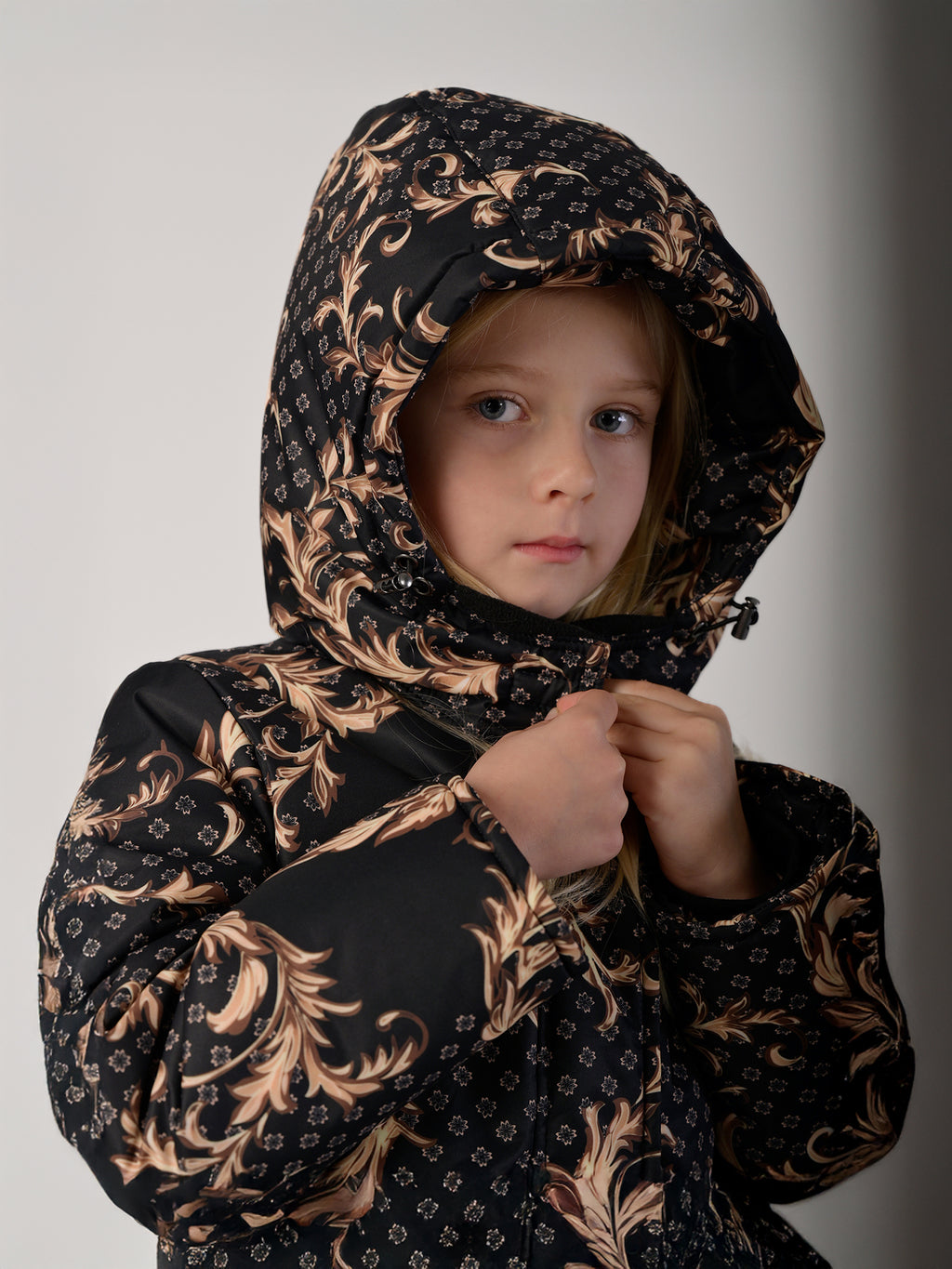 Luxury girls’ snowsuit with golden baroque print on black, handcrafted in Europe from waterproof polyester with Sorona® plant-based insulation. Warm and breathable winter overall for kids, certified Oeko-Tex Standard 100, perfect for skiing and cold weather up to −25°C.