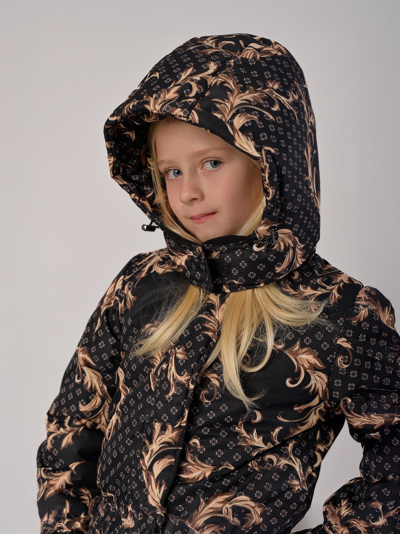 Luxury girls’ snowsuit with golden baroque print on black, handcrafted in Europe from waterproof polyester with Sorona® plant-based insulation. Warm and breathable winter overall for kids, certified Oeko-Tex Standard 100, perfect for skiing and cold weather up to −25°C.
