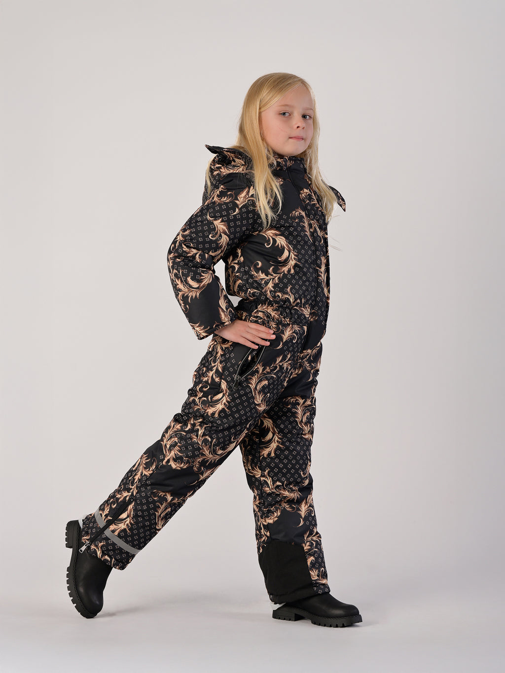 Luxury girls’ snowsuit with golden baroque print on black, handcrafted in Europe from waterproof polyester with Sorona® plant-based insulation. Warm and breathable winter overall for kids, certified Oeko-Tex Standard 100, perfect for skiing and cold weather up to −25°C.