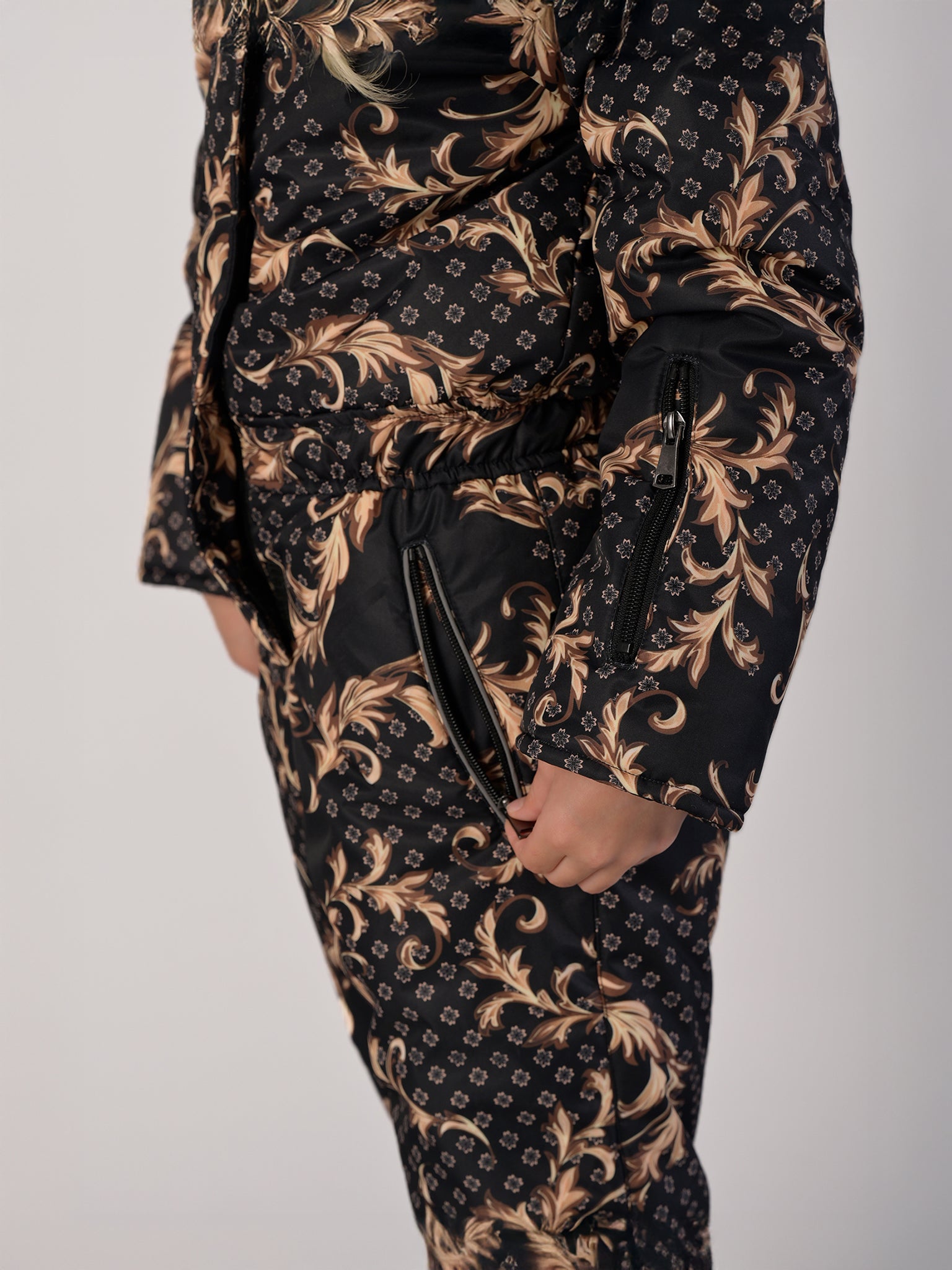 Luxury girls’ snowsuit with golden baroque print on black, handcrafted in Europe from waterproof polyester with Sorona® plant-based insulation. Warm and breathable winter overall for kids, certified Oeko-Tex Standard 100, perfect for skiing and cold weather up to −25°C.